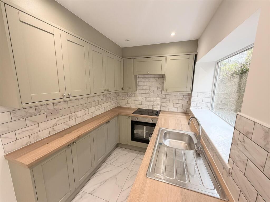 Galley kitchen in sage shaker units with oak worktops and metro tiling